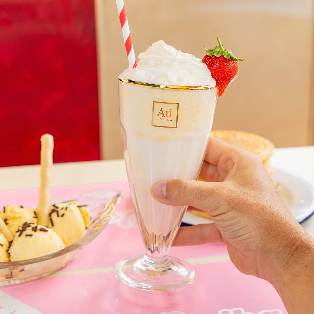 Hand holding an Au Vodka Strawberry Milkshake with whipped cream and a strawberry garnish