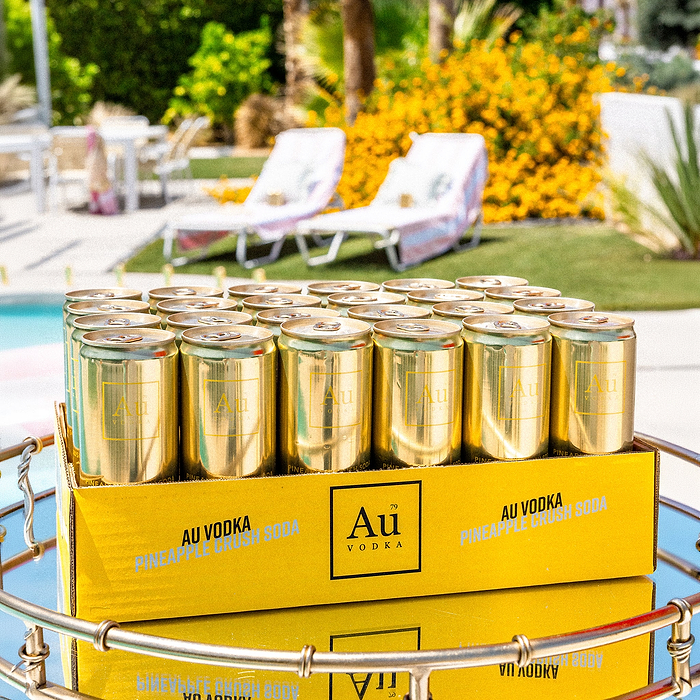 Au Vodka Pineapple Crush Soda cans in a yellow box by a pool