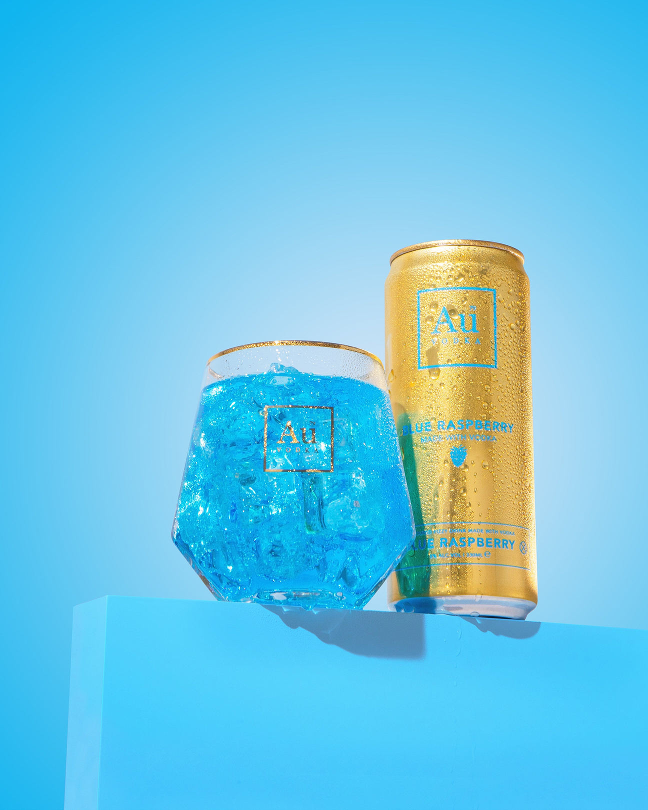 Au Vodka Blue Raspberry can and glass with blue drink and ice on blue pedestal