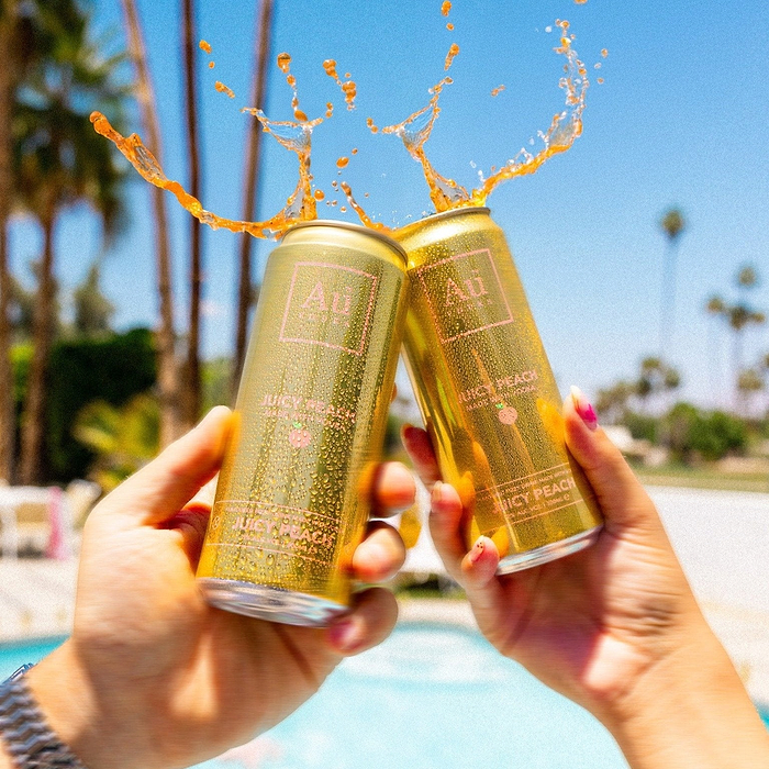 Two Au Vodka USA Juicy Peach cans clinking with liquid splashing out, poolside