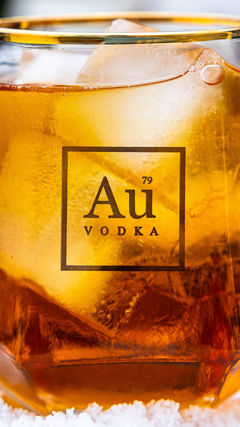 Au Vodka logo on a glass filled with amber liquid and ice cubes