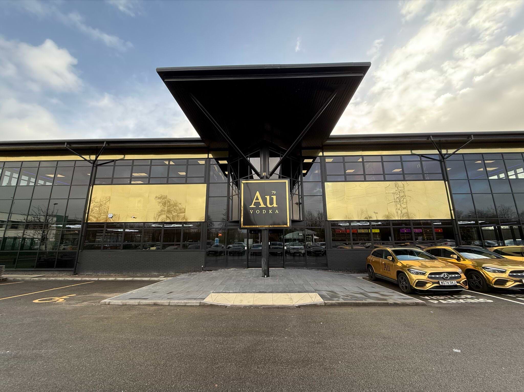 Au Vodka building exterior with gold-tinted windows and black facade, gold Mercedes cars parked outside