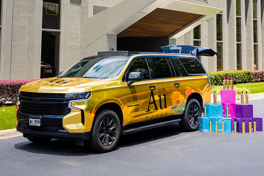 Gold Au Vodka branded SUV with open trunk, surrounded by stacks of colorful Au Vodka boxes and bottles