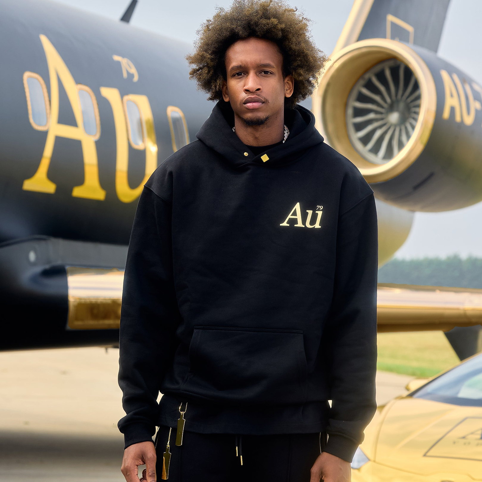 Man wearing black Au Vodka apparel hoodie with gold logo in front of private jet