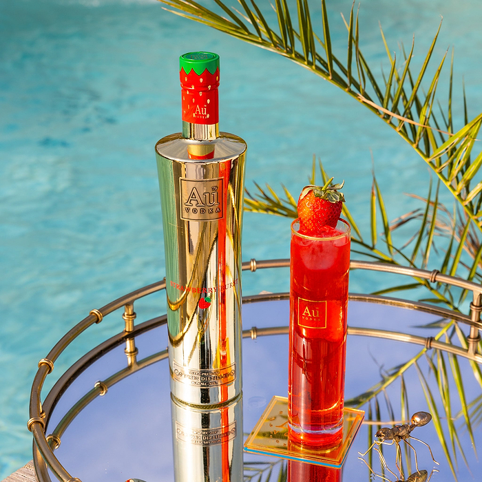 Au Vodka Strawberry Burst bottle and branded glassware with a strawberry garnish on a mirrored tray