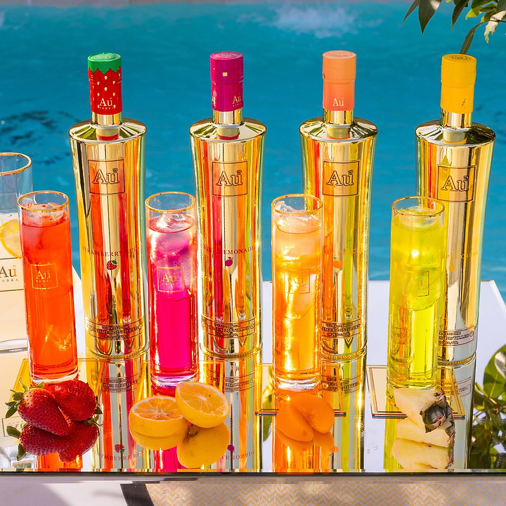 Au Vodka bottle bundle featuring Juicy Peach and other flavors with matching cocktails on a reflective surface