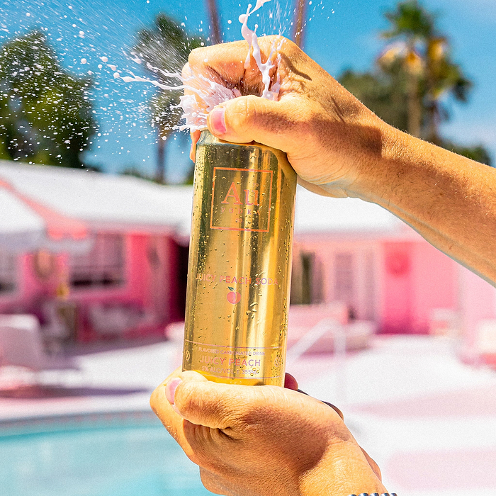Hands opening an Au Vodka USA Juicy Peach can with liquid splashing out