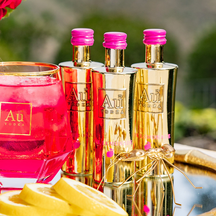 Three Au Vodka USA Pink Lemonade bottles with a pink drink in a glass and lemon slices