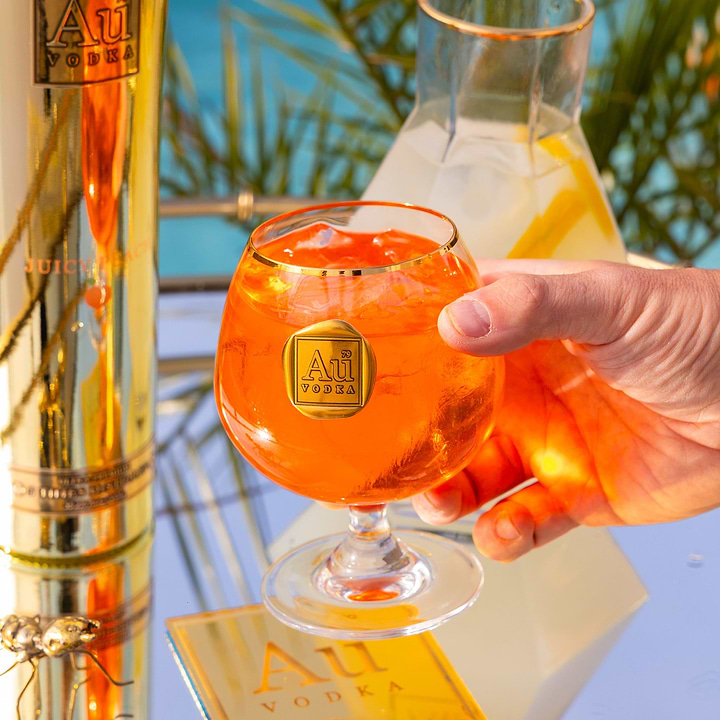 Hand holding an Au Vodka branded glass filled with an orange cocktail and ice
