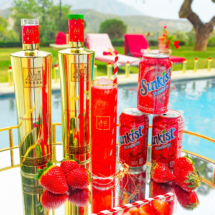 Au Vodka Strawberry Burst 750ml bottles, Sunkist Strawberry Soda cans, and fresh strawberries on a tray
