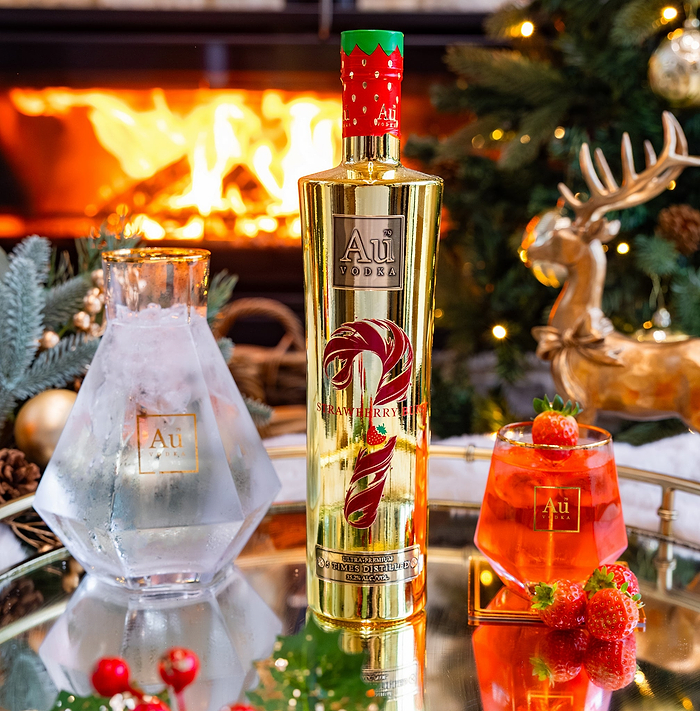 Gold bottle of Au Vodka with a red candy cane design, surrounded by festive decor including a Christmas tree and fireplace.