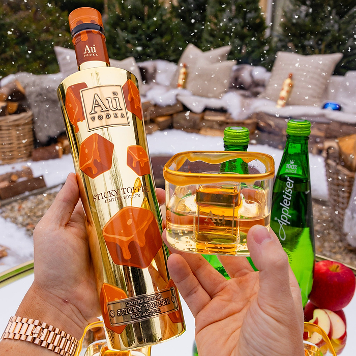Person holding a bottle of Au Vodka Sticky Toffee and a bomb glass with Appeltiser. 