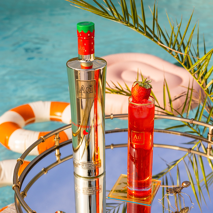 Au Vodka USA Strawberry Burst bottle and glass with a strawberry garnish on a mirrored tray by a pool