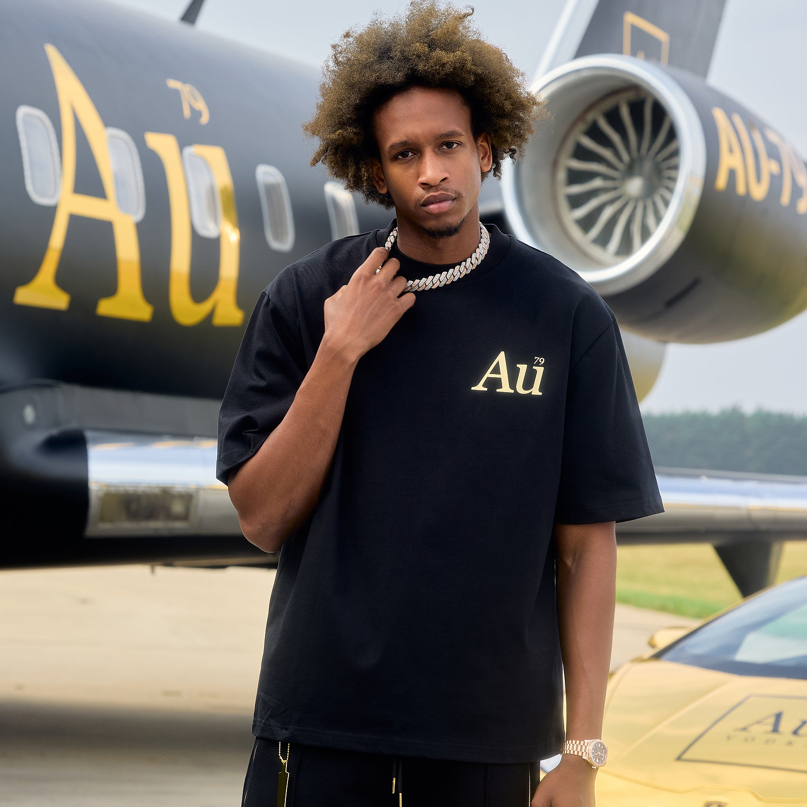 Person wearing black Au Vodka apparel t-shirt with gold logo in front of private jet