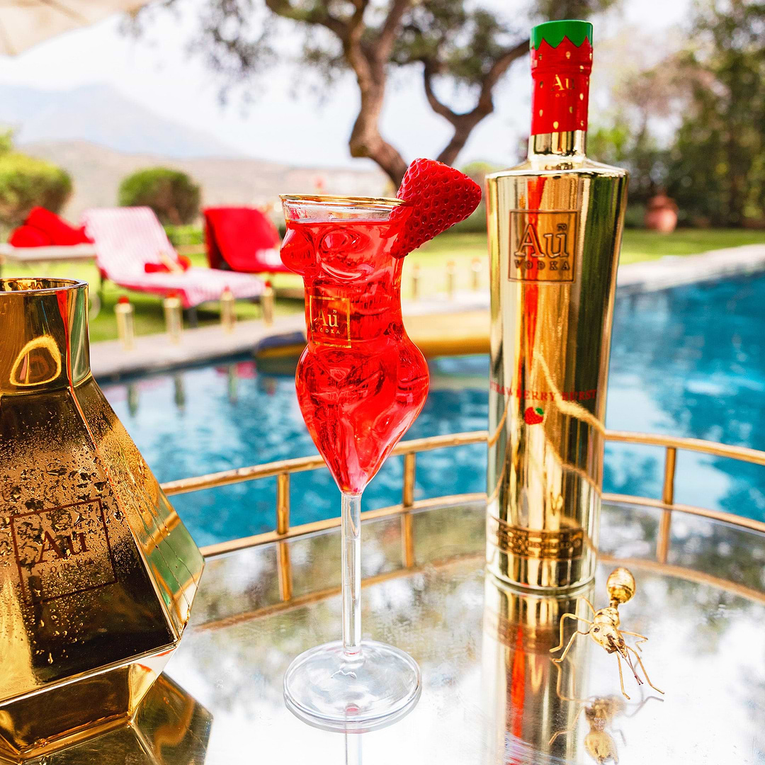 Au Vodka Strawberry Burst bottle and red cocktail in a shaped glass on a poolside table