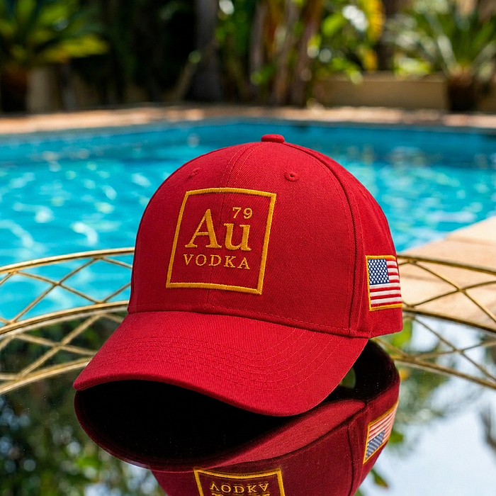 Au Vodka USA red baseball cap with gold logo and US flag patch, reflected on a mirrored surface by a pool