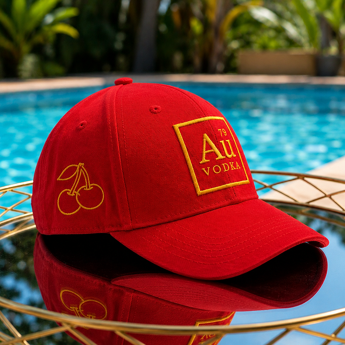 Red Au Vodka USA baseball cap with gold cherry embroidery on a reflective surface by a pool