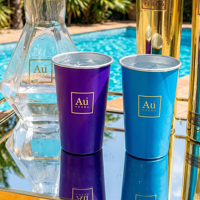 Au Vodka USA merchandise: purple and blue cups with Au Vodka logo, next to a clear bottle by a pool