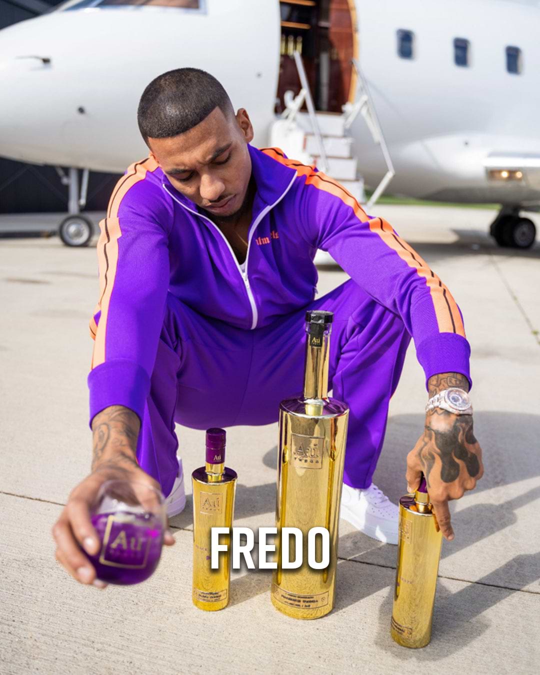 Fredo in a purple tracksuit with Au Vodka bottles and a private jet in the background