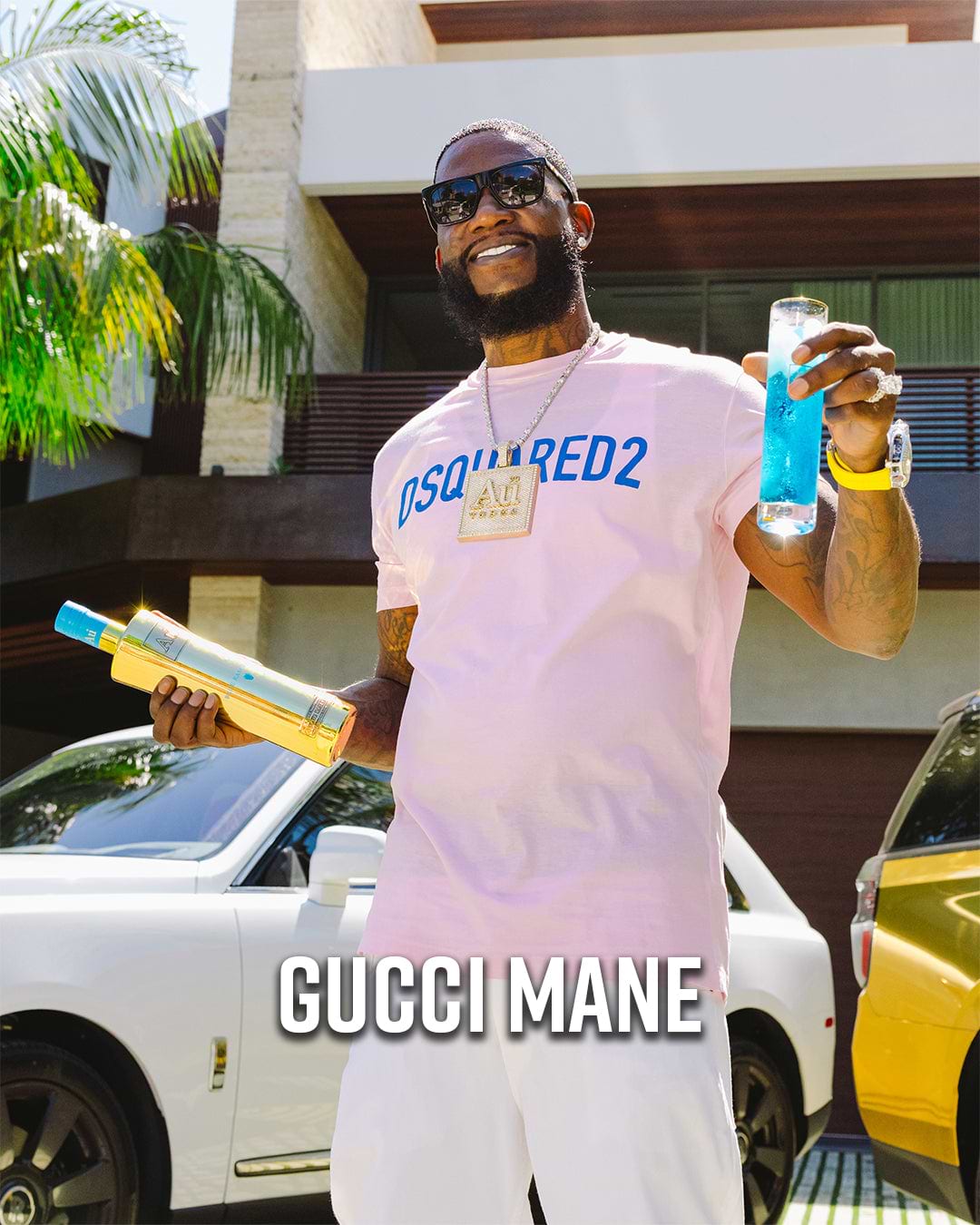 Gucci Mane in a pink shirt and white shorts, holding a gold bottle and a blue drink