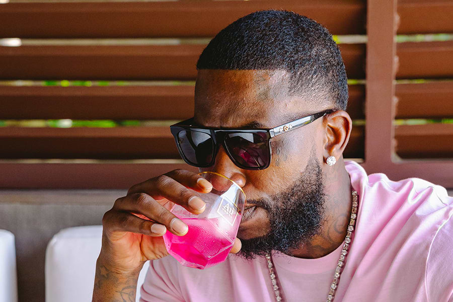 Man in sunglasses and pink shirt drinking a pink beverage from a glass
