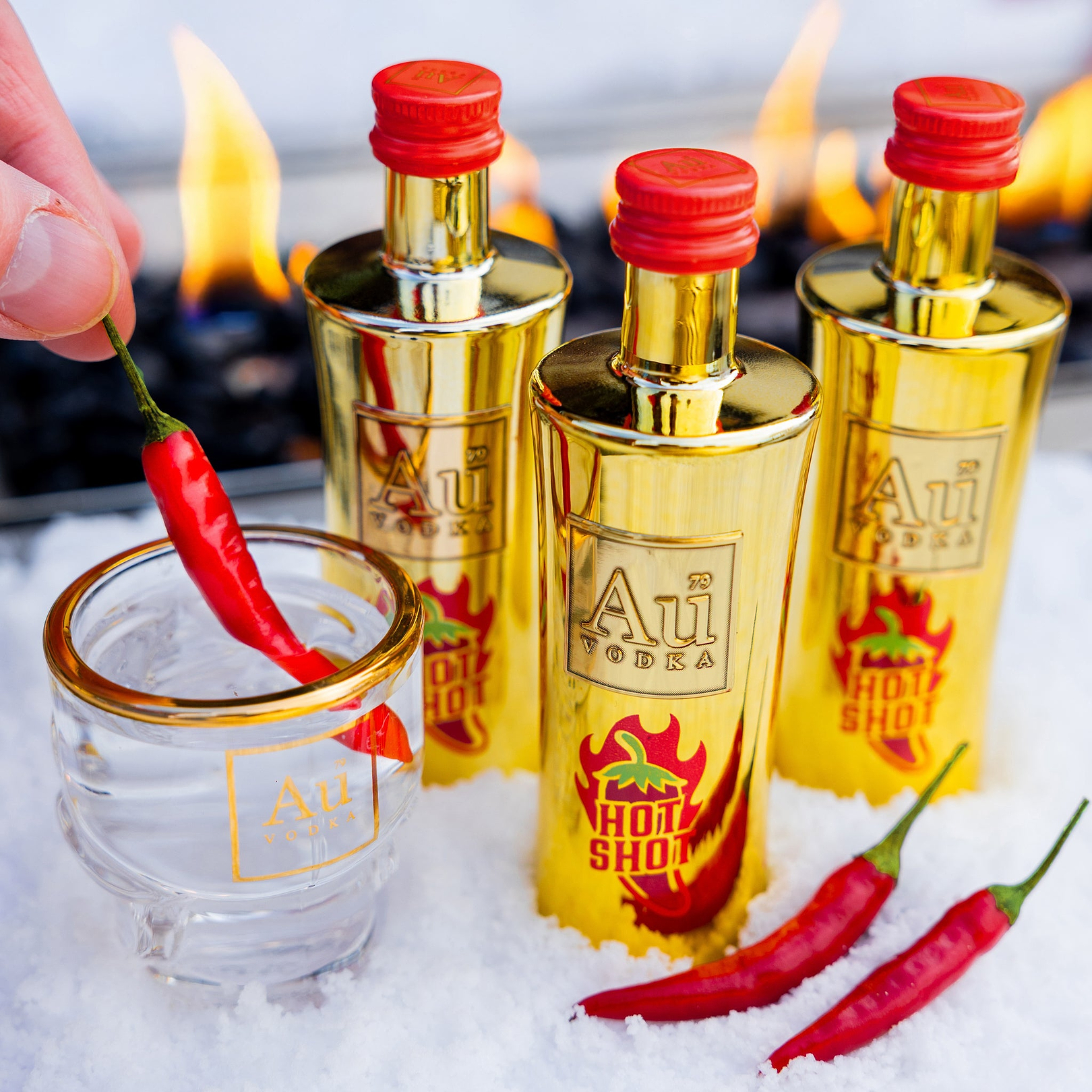 Au Vodka Hot Shot gold bottles and shot glass with red chili peppers in snow