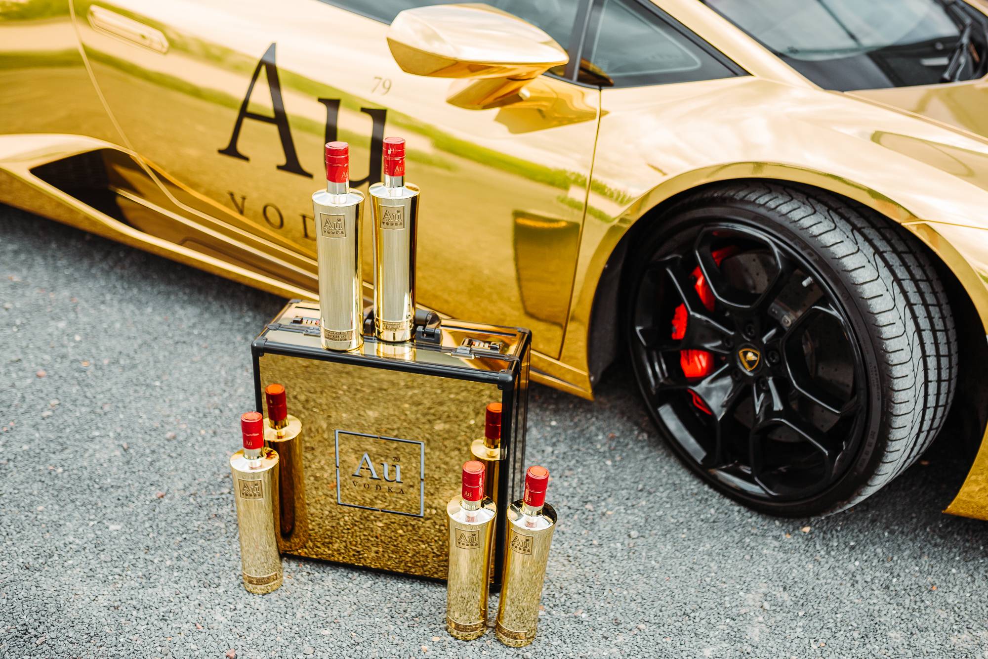 Au Vodka bottles and branded display case in front of a gold Lamborghini
