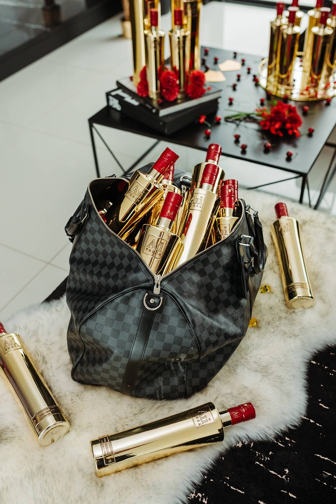 Au Vodka gold bottles inside a black checkered duffel bag on a white faux fur rug
