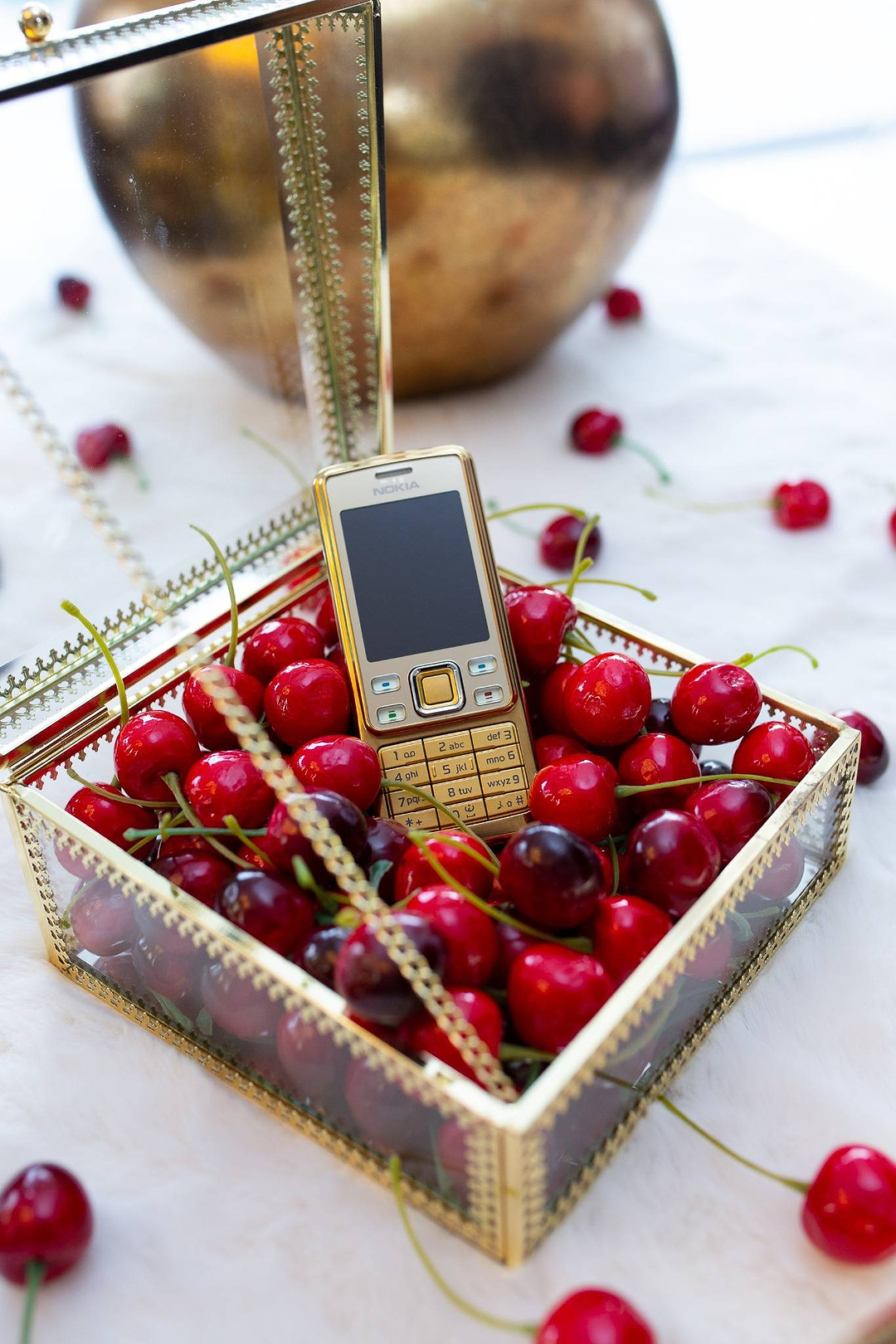 Gold Nokia mobile phone inside a glass box filled with fresh red cherries
