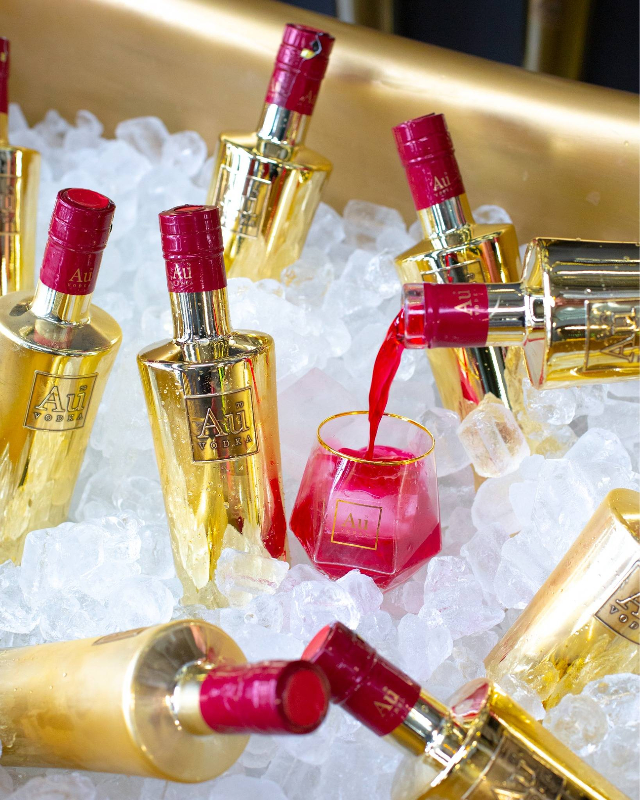 Au Vodka bottles in gold packaging being poured into a glass over ice