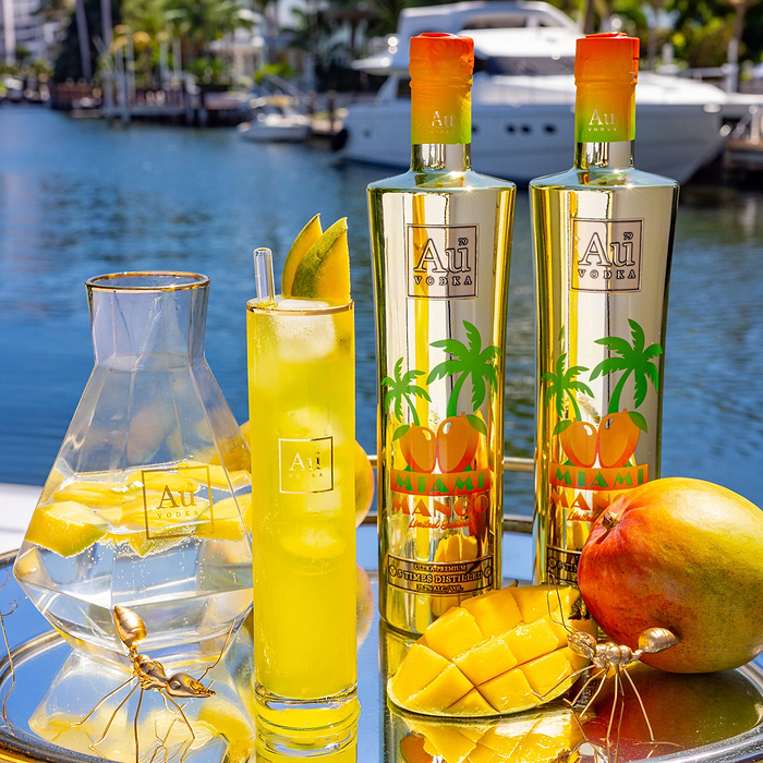 Au Vodka USA Mango Passion bottles and drinks on a tray with mangoes by a canal