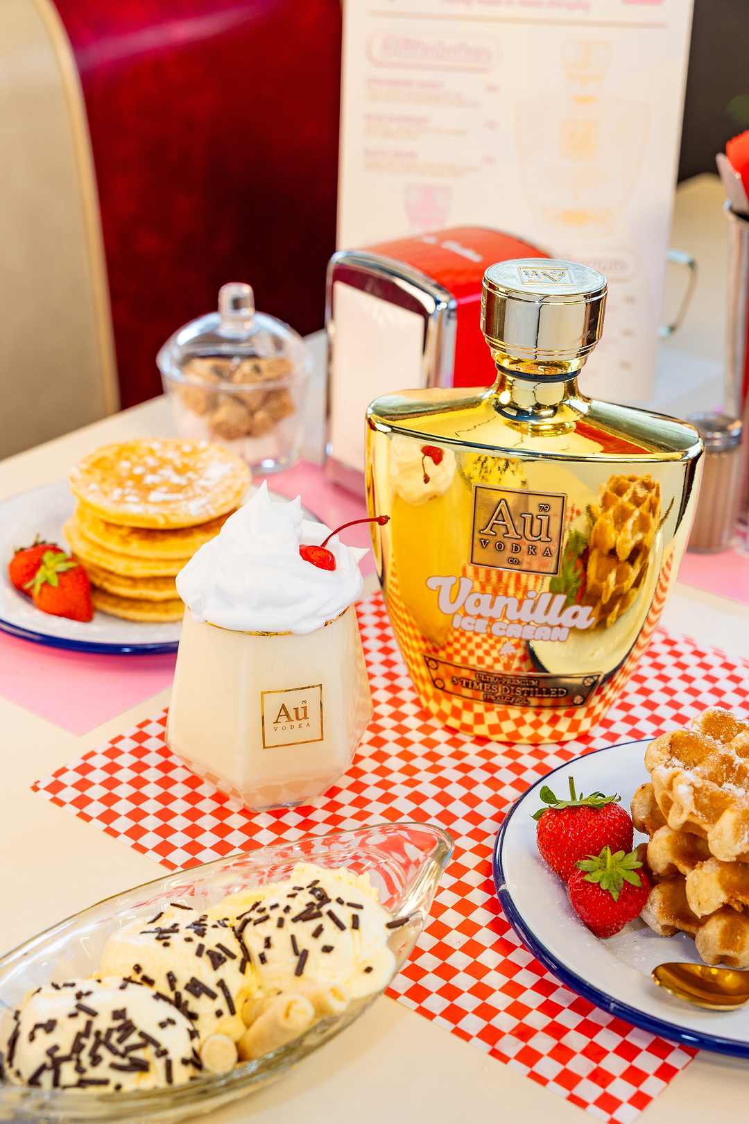 Au Vodka Vanilla Ice Cream bottle with a cocktail and dessert on a red and white checkered table