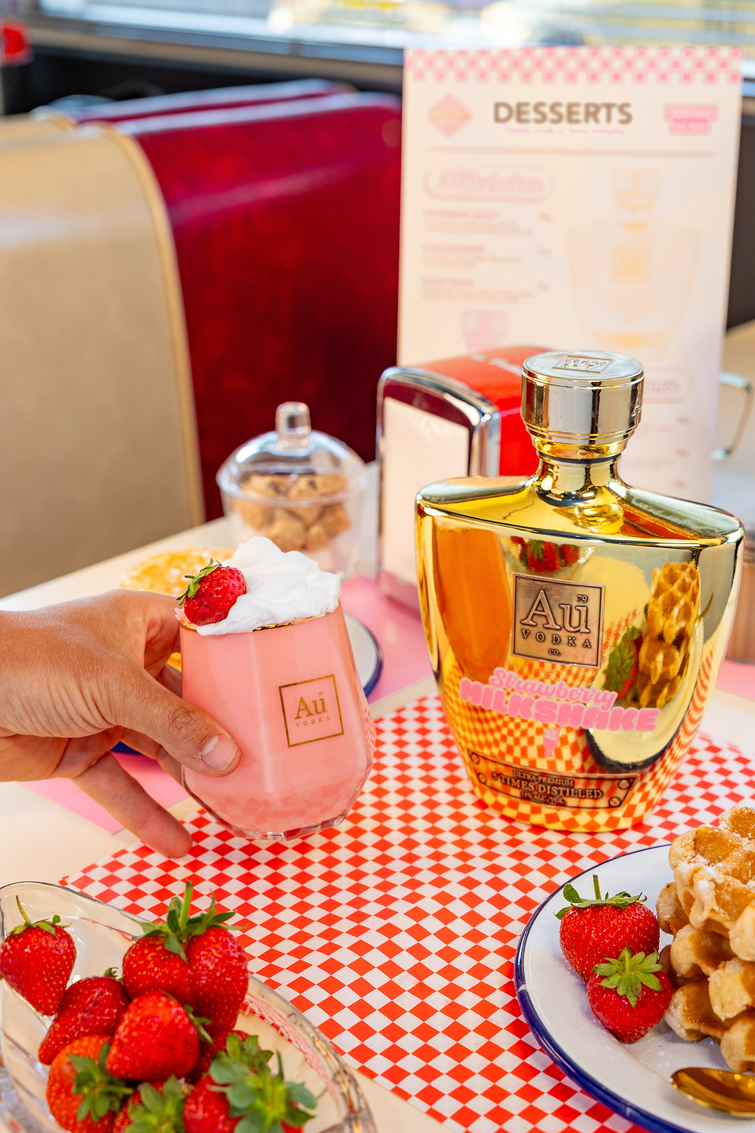 Au Vodka Strawberry Milkshake bottle and glass with whipped cream and strawberry on a diner table