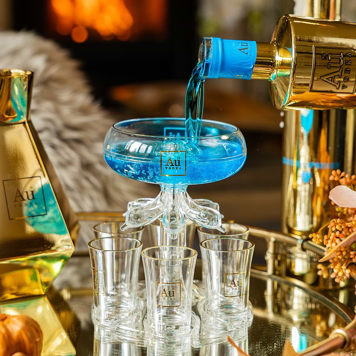 Au Vodka bottle pouring blue liquid into a glass shot tower on a mirrored tray