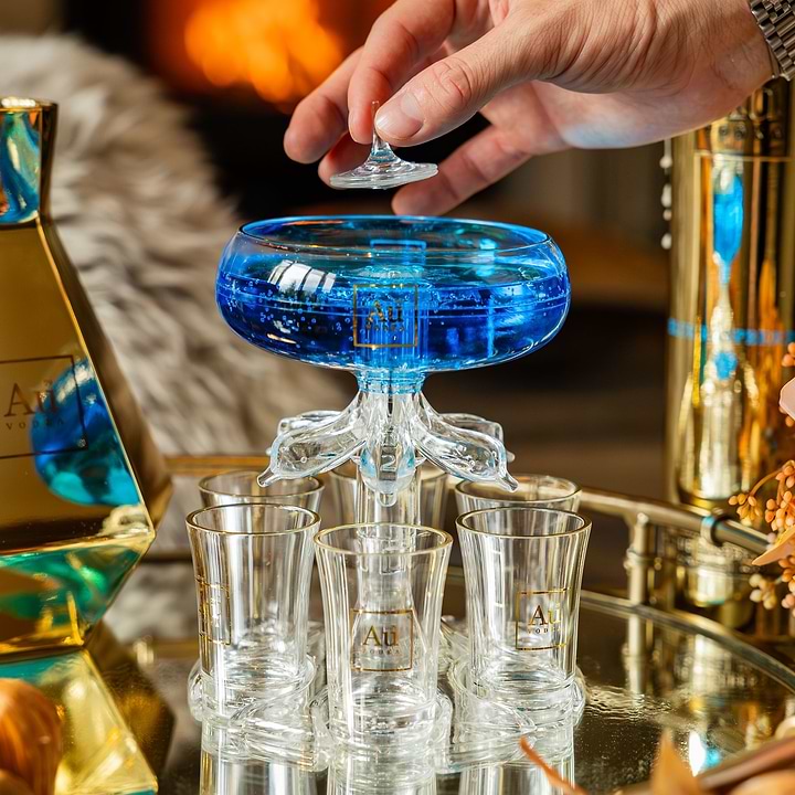 Hand placing a glass stopper on an Au Vodka shot tower filled with blue liquid on a mirrored tray