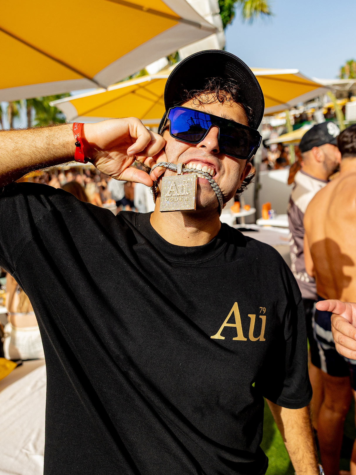 Man wearing a black Au Vodka t-shirt and holding a diamond Au Vodka pendant in his mouth