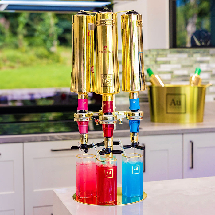 Au Vodka merchandise triple bottle dispenser with three glasses of colorful cocktails on a kitchen counter