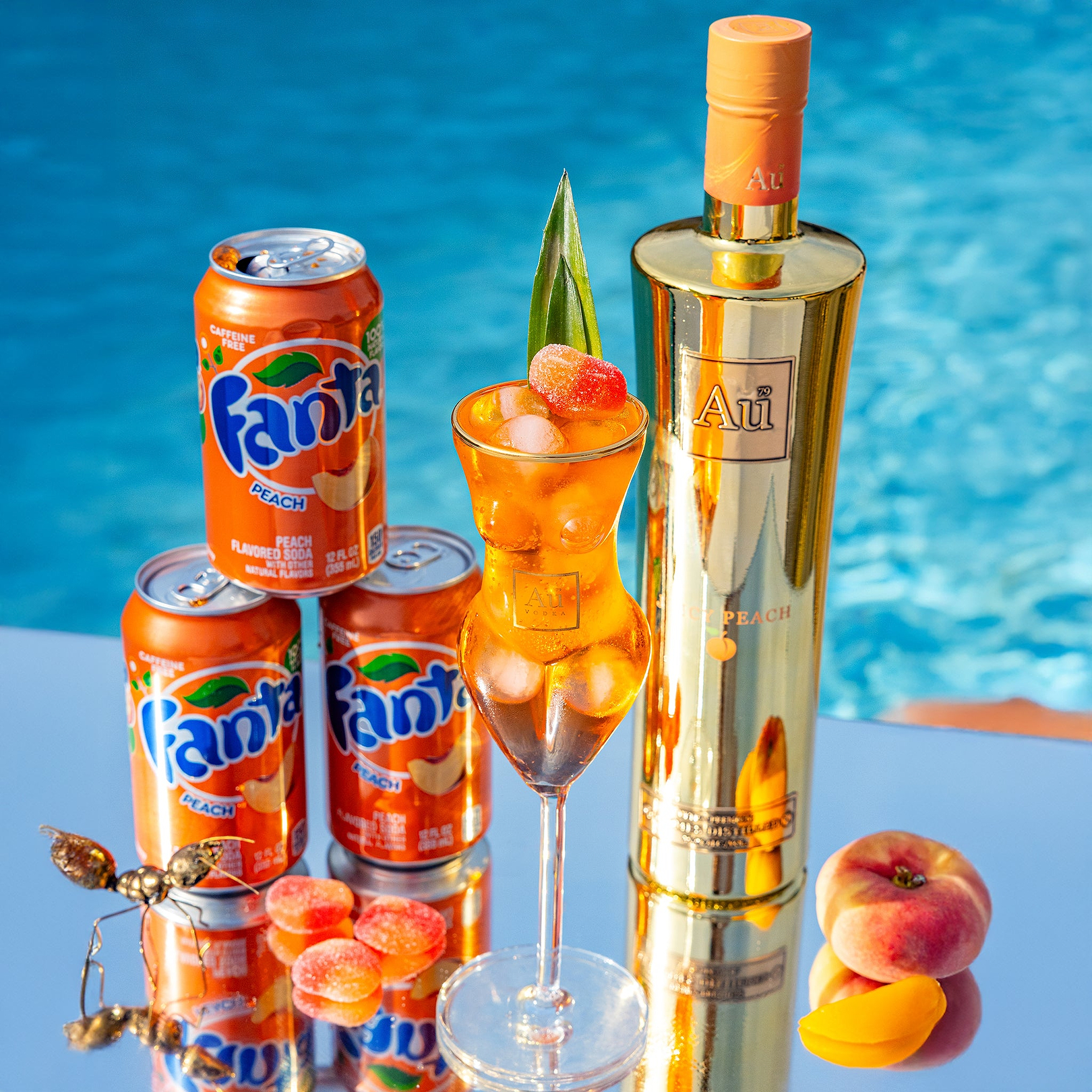 Au Vodka Juicy Peach bottle with Fanta Peach cans and a cocktail garnish by a pool
