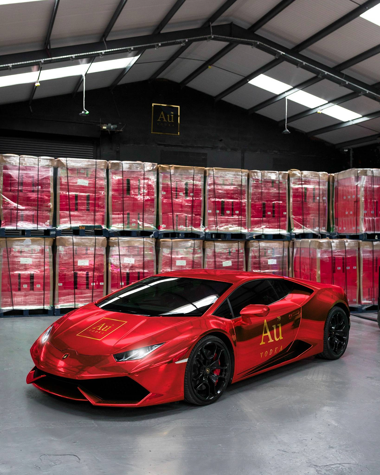 Red chrome Lamborghini parked in a warehouse with stacked pallets of Au Vodka