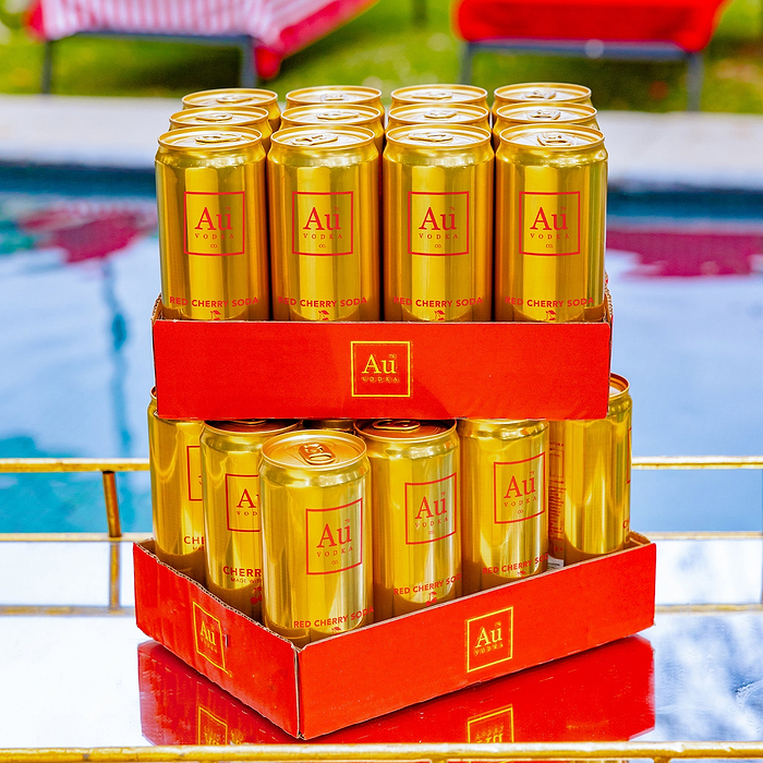 Two red trays with Au Vodka USA Red Cherry Soda cans, twelve cans total, by a pool