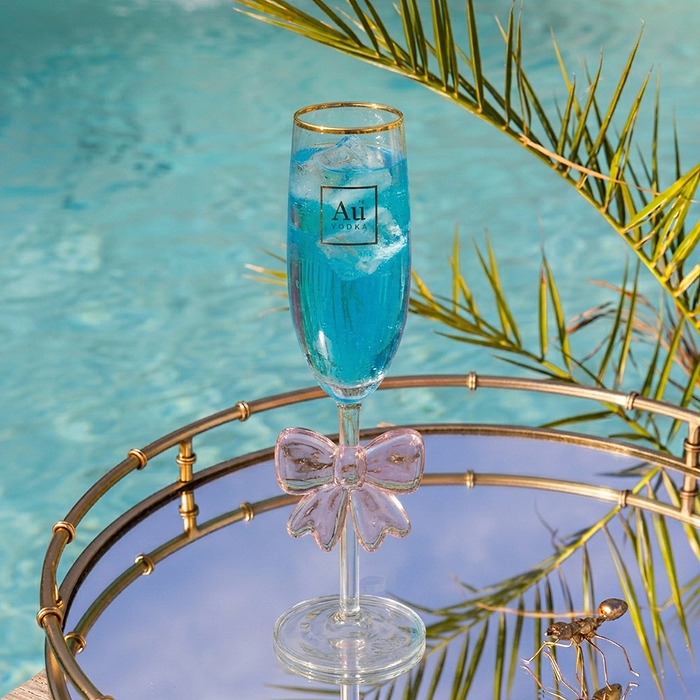 Au Vodka USA glassware with blue drink and ice, gold rim, and bow detail on stem, on a mirrored tray