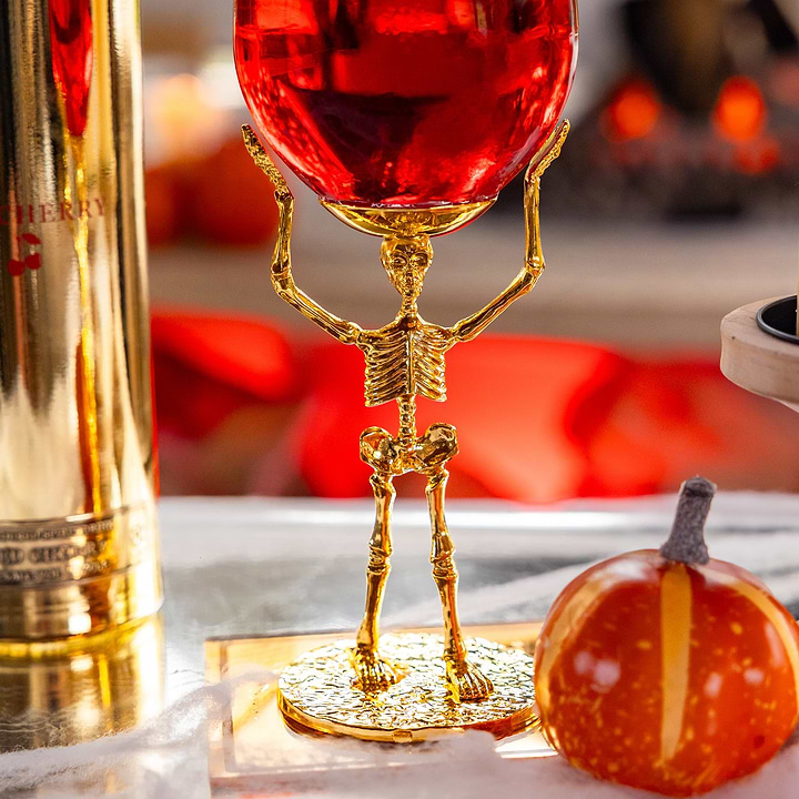 Au Vodka gold skeleton stemware glass filled with red liquid next to a small pumpkin
