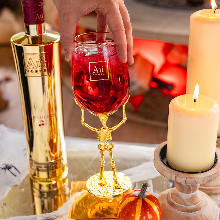 Au Vodka branded skeleton stem glassware filled with red cocktail next to gold bottle and candles