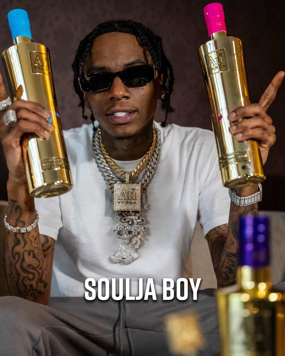 Soulja Boy holding two gold Au Vodka bottles, one with a blue cap and one with a pink cap