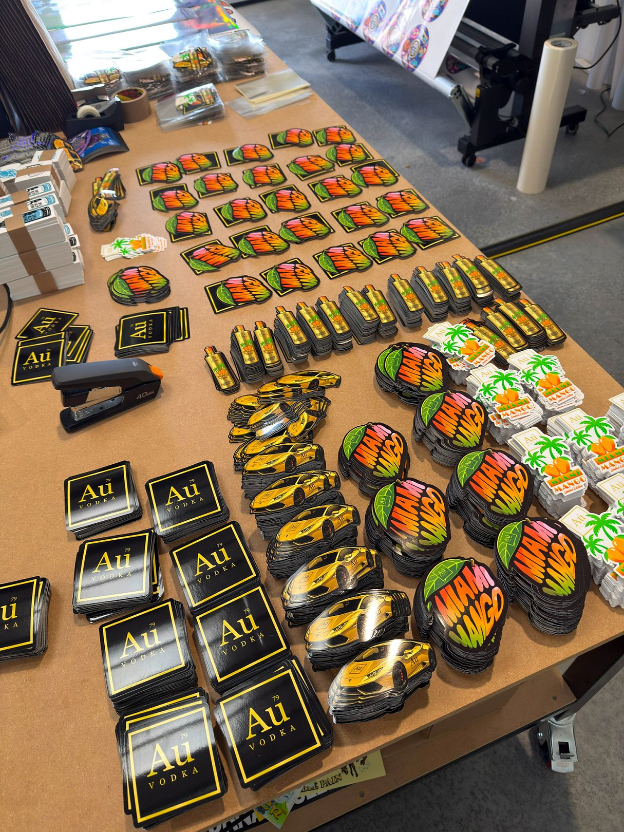 Table with various custom-shaped stickers including Au Vodka, Miami Mango, and gold sports cars