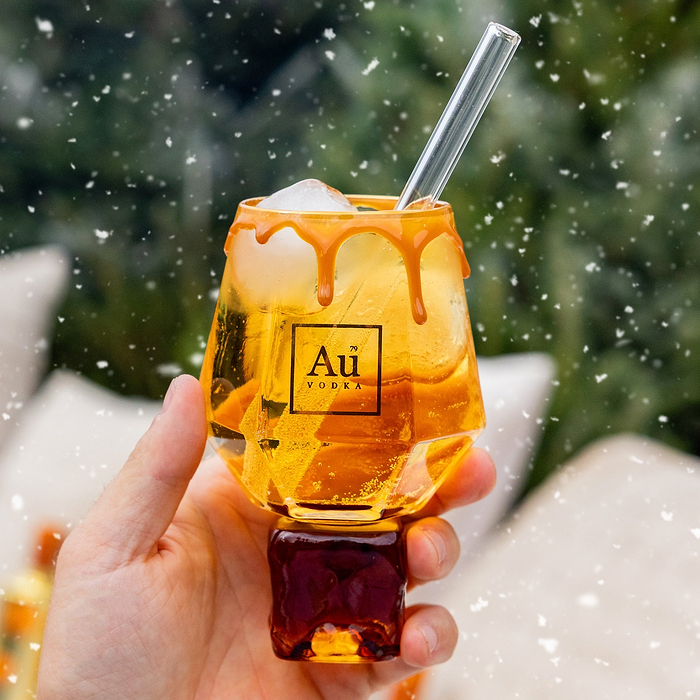 Hand holding a glass of peach flavored liquid with a straw, against a snow and christmas style background.