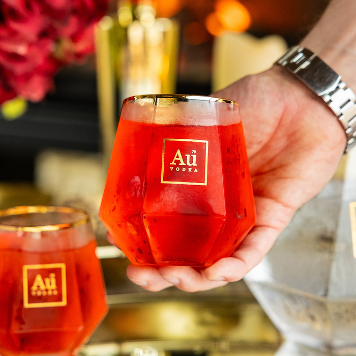 Hand holding a faceted glass filled with red Au Vodka cocktail