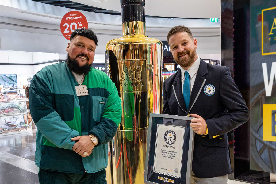 Two men stand next to a giant gold Au Vodka bottle, holding a Guinness World Records certificate