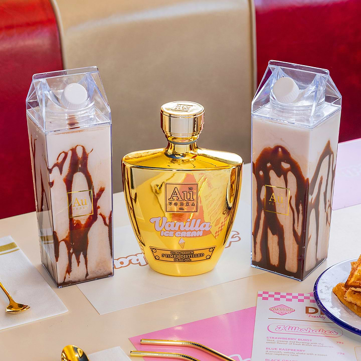 Two clear cartons of chocolate drink flanking a gold Au Vodka bottle
