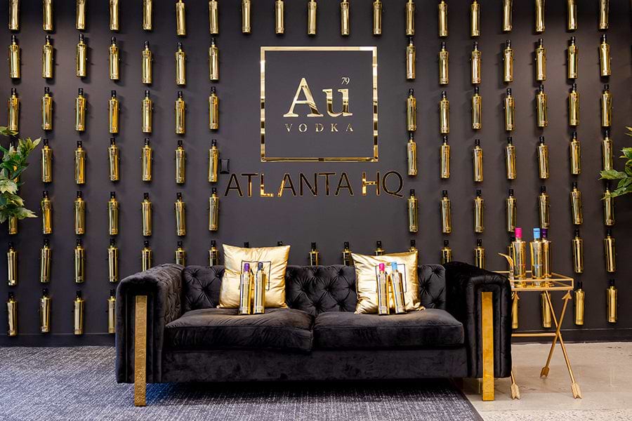 Au Vodka Atlanta HQ with gold bottles on wall, black sofa, and gold pillows